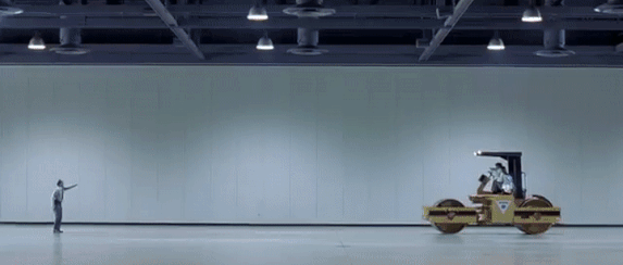 GIF of a humorous scene in Austin Powers where a guard desperately pleads for a slowly moving steamroller to stop instead of moving out of its way.